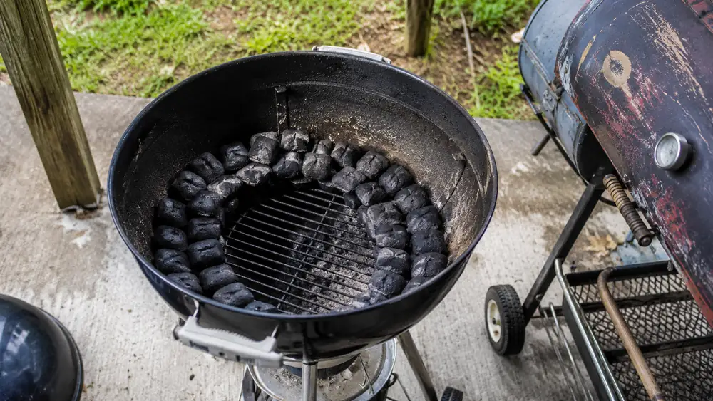 A ring of charcoal briquettes arranged in an overlapping snake pattern inside an open kettle grill before lighting