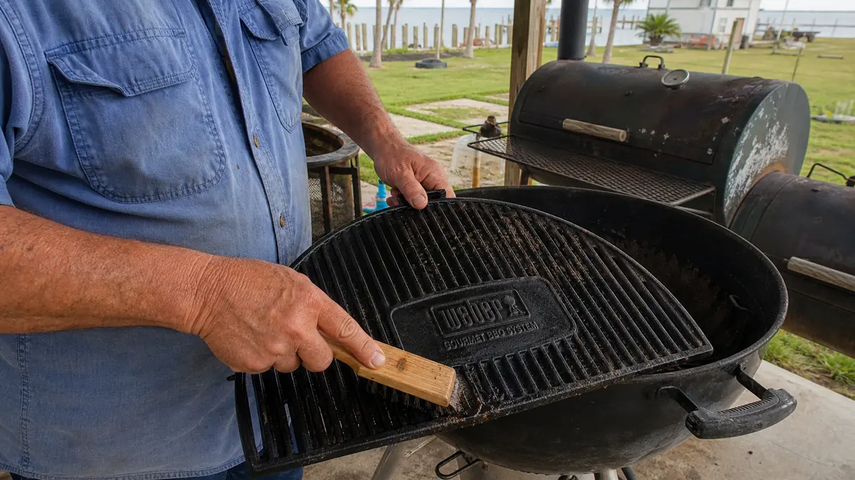Hands using a bamboo scraper to clean burger fat out of the ridges of a black cast iron sear grate after a cook